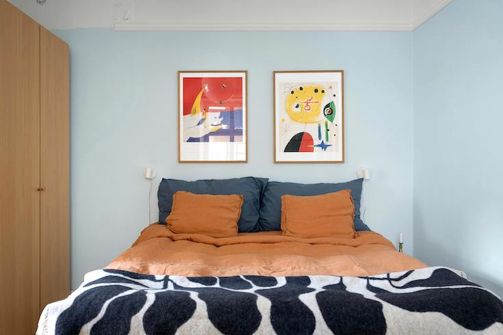 Bright modern wall art on a blue wall in a bedroom above a bed with orange, teal, black and white bedding and blankets