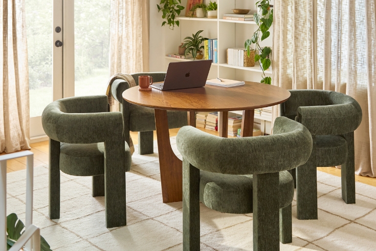 Bright living room featuring wooden round table and four green velvet dining chairs from Article.